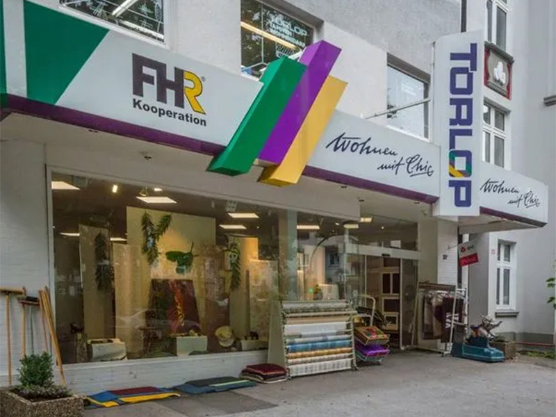 Eingang des Fachgeschäfts Torlop in Dortmund mit Schaufensterfront, Ladenschild und einladendem Bodenbelag-Design.